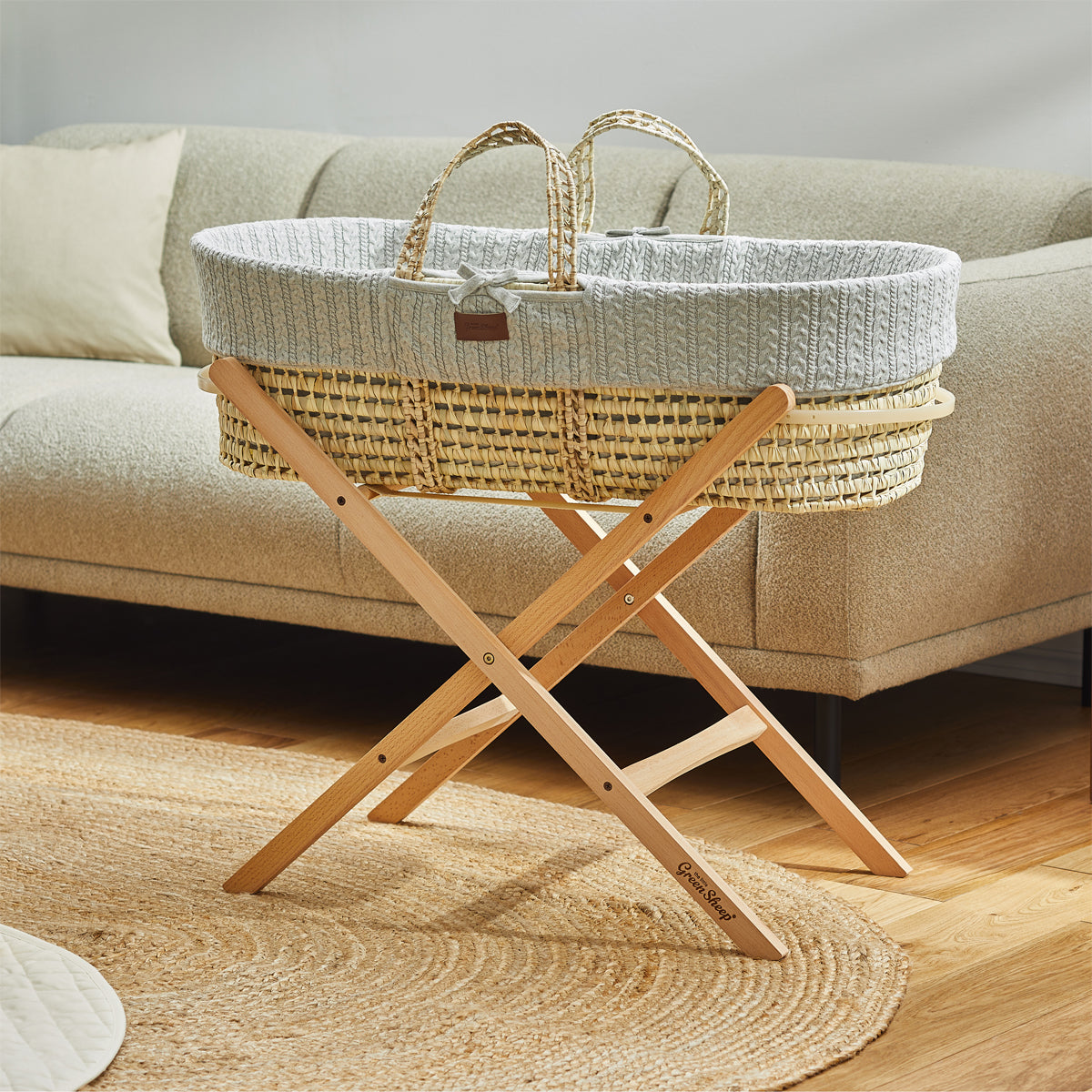 A baby's Dove Moses basket on a wooden stand, situated in front of a couch