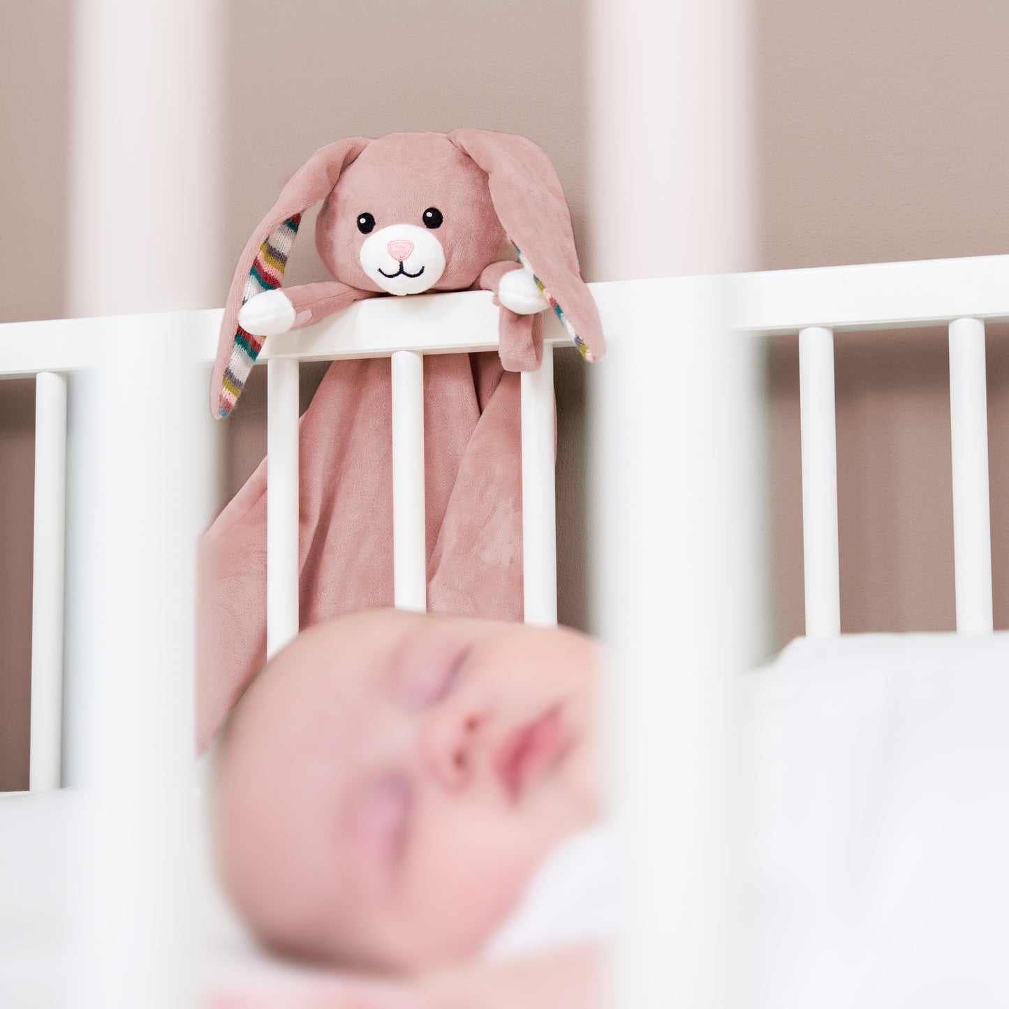 A pink bunny baby comforter attached to a cot bed, while the baby sleeps.