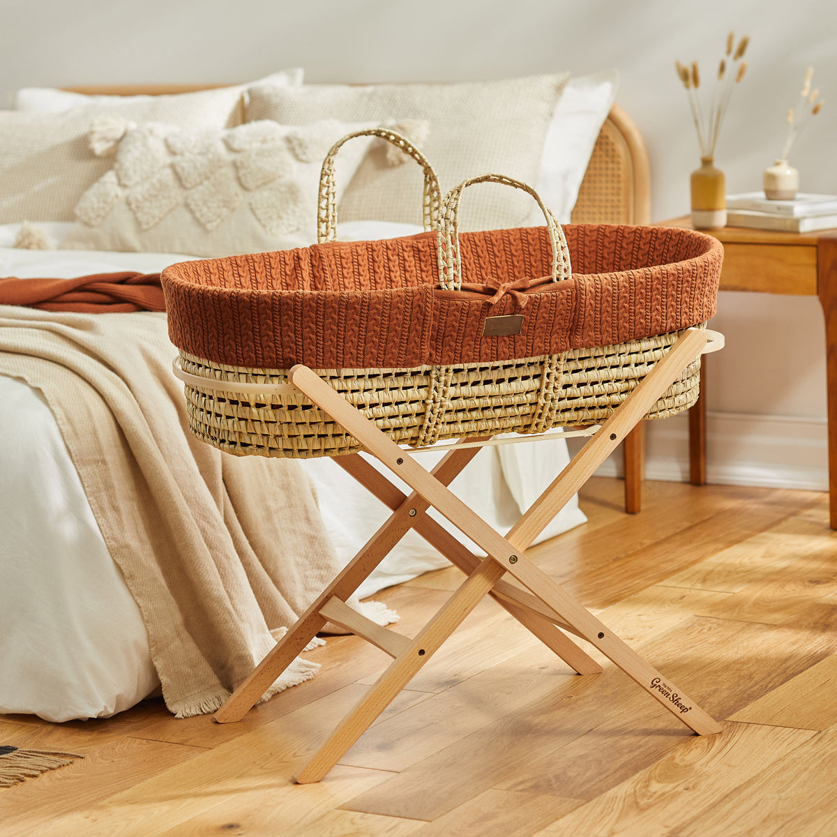  A baby's terracotta Moses basket on a wooden stand, situated in front of a double bed