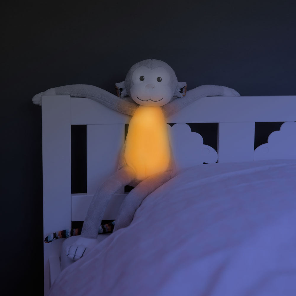 A grey and white monkey illustrating its sound and lighting functions, while attached to a toddlers bed.