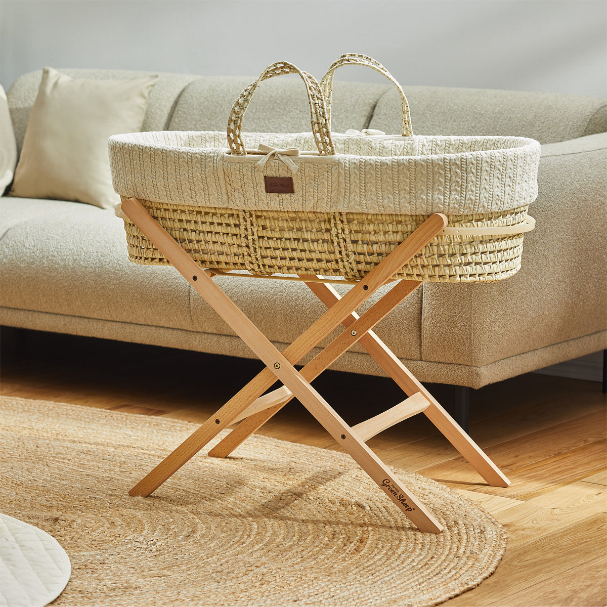  A baby's linen Moses basket on a wooden stand, situated in front of a couch