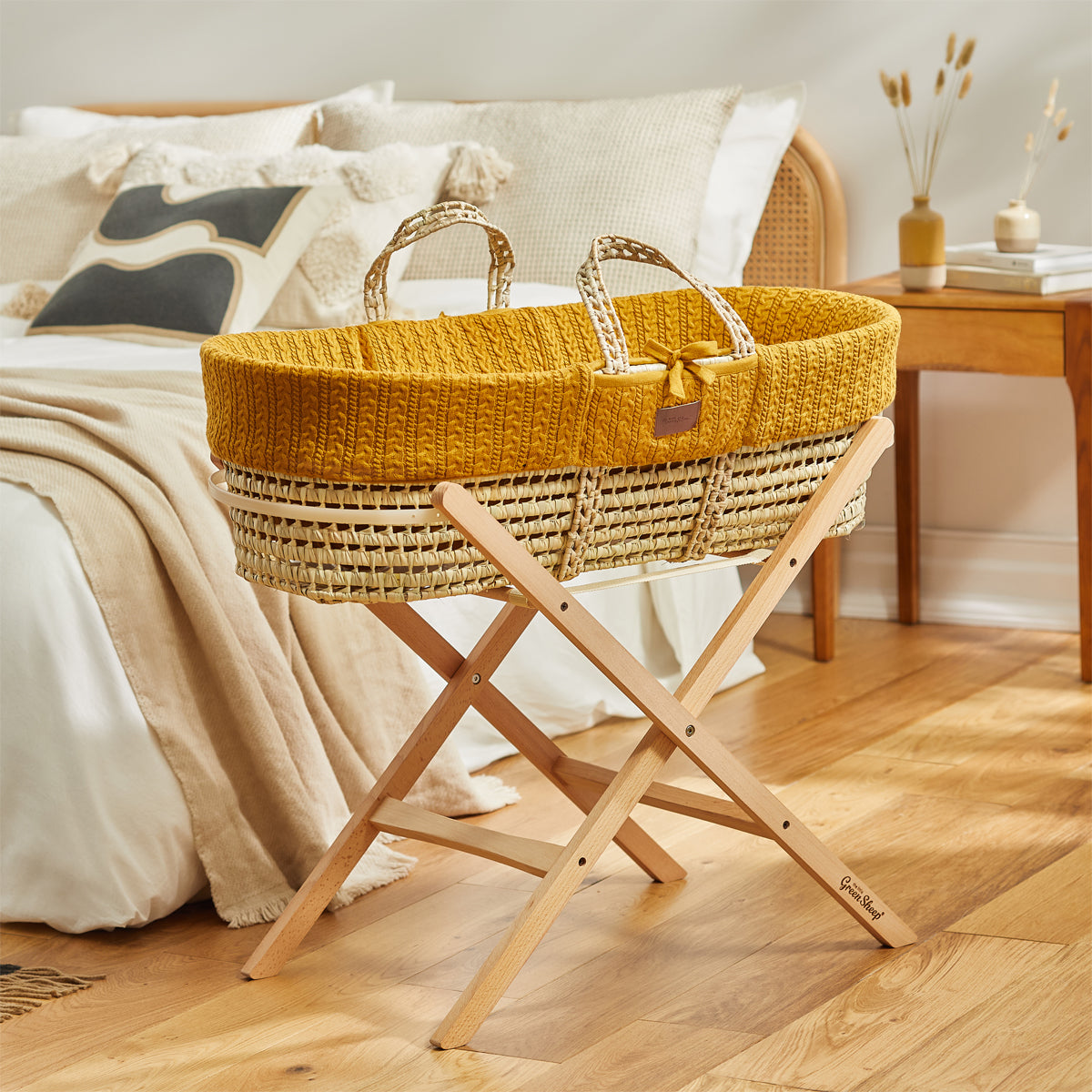  A baby's Honey Moses basket on a wooden stand, situated in front of a double bed