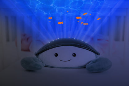 A teal and white crab shaped projector, sitting on a bedside locker displaying night light colours, while the baby rests in their cot.