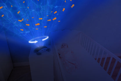 A teal and white crab shaped projector, sitting on a bedside locker displaying night light colours, while the baby rests in their cot.