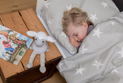 A grey and white sheep illustrating its lighting features while a toddle sleeps in their bed.