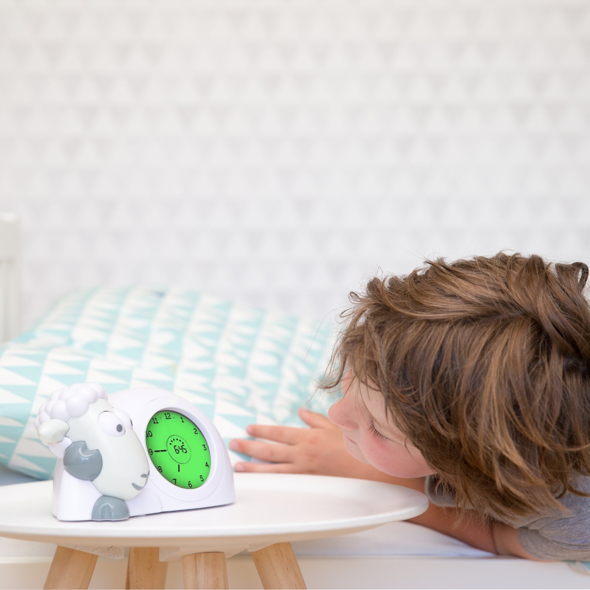 A white a grey sheep with a clock in its belly showing the different colours of its belly when the time changes, while a toddler reads the time in the background.