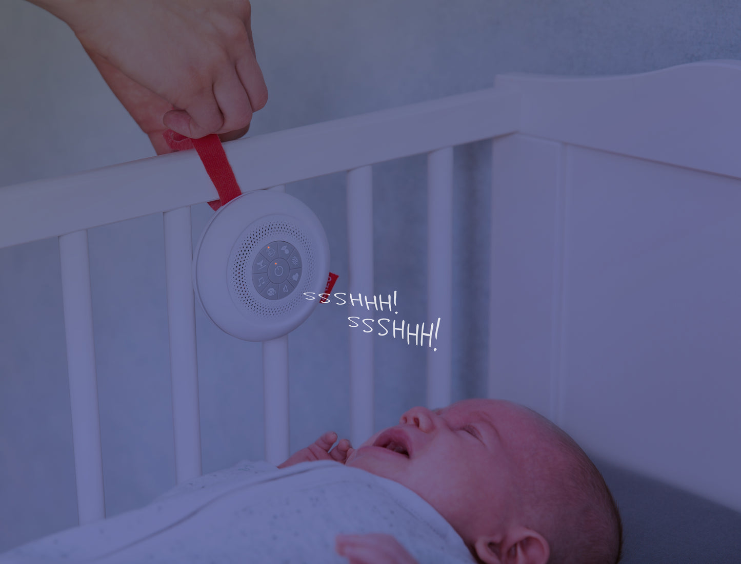 A round sound box with multiple feature buttons and red attachment strap, hanging on a cot bed playing sounds while a baby cries.