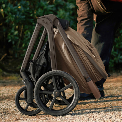 A multi-piece silver cross cove 2 travel system set in taupe brown and black, displayed on white pedestals against a white background. The set includes a stroller, bassinet, car seat in taupe, infant seat, footmuff, backpack, car seat liner, and accessories.