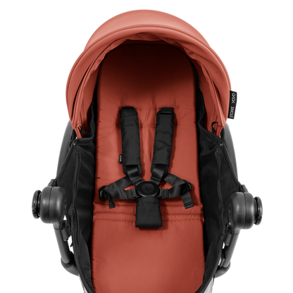 A black stroller newborn travel system shown in terracotta, with a stroller behind it to demonstrate compatibility, on a clean white background.