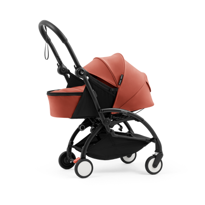 A yoyo stroller bassinet attachment set in terracotta orange and black, shown mounted on a stroller frame against a solid white background.