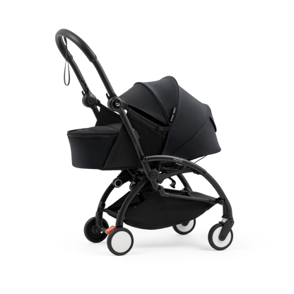 A black stroller newborn travel system shown in black, with a stroller behind it to demonstrate compatibility, on a clean white background.