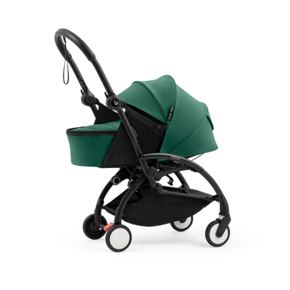 A black stroller newborn travel system shown in green, with a stroller behind it to demonstrate compatibility, on a clean white background.