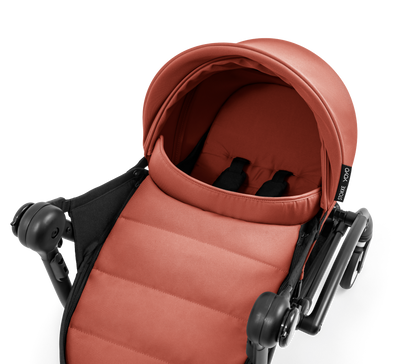 A yoyo stroller bassinet attachment set in terracotta orange and black, shown mounted on a stroller frame against a solid white background.