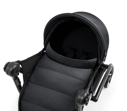 A black stroller newborn travel system shown in black, with a stroller behind it to demonstrate compatibility, on a clean white background.