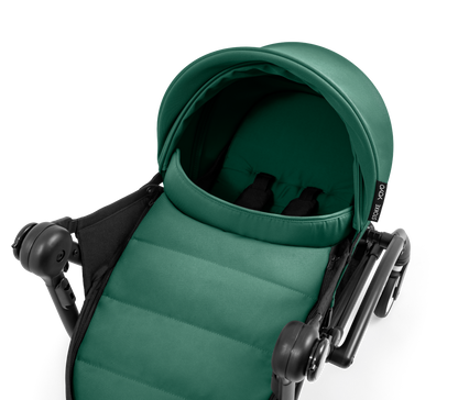 A black stroller newborn travel system shown in green, with a stroller behind it to demonstrate compatibility, on a clean white background.