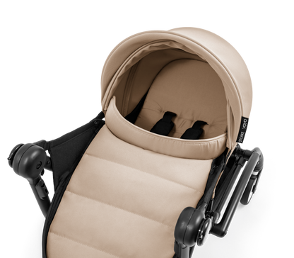 A yoyo stroller bassinet attachment set in beige and black, shown mounted on a stroller frame against a solid white background.