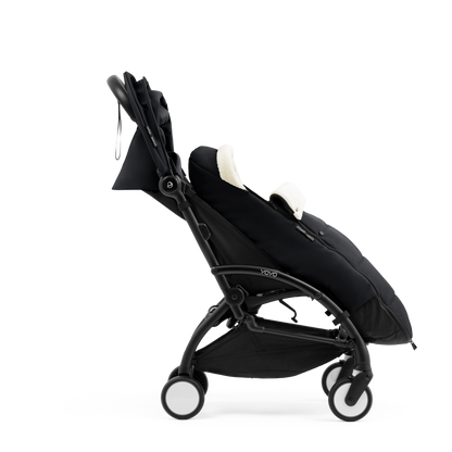 A stroller with a black colored padded footmuff, cream fleece lining, and a black frame, shown from the front on a white background.