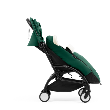 A stroller with a forest green colored padded footmuff, cream fleece lining, and a black frame, shown from the front on a white background.