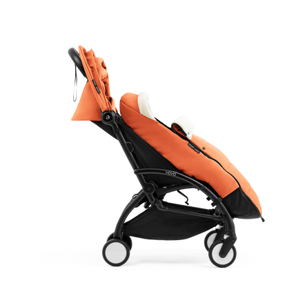 A stroller with a orange colored padded footmuff, cream fleece lining, and a black frame, shown from the front on a white background.
