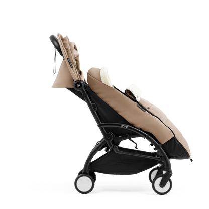 A stroller with a beige colored padded footmuff, cream fleece lining, and a black frame, shown from the front on a white background.