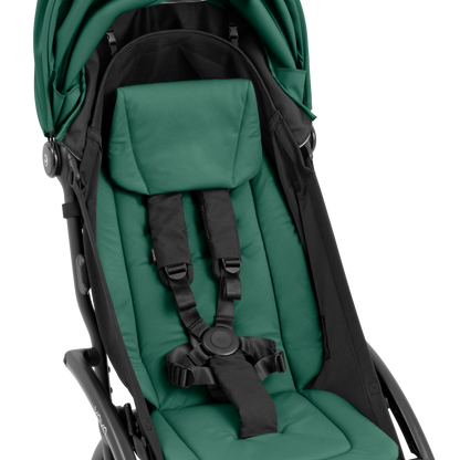 A compact baby stroller with a dark green canopy and dark green padded seat, with a blacked out chassis, shown on a plain white background.