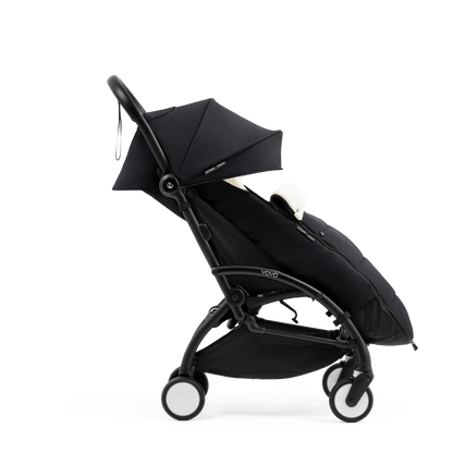 A stroller with a black colored padded footmuff, cream fleece lining, and a black frame, shown from the front on a white background.