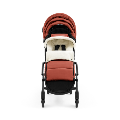 A stroller with a rust-colored padded footmuff, cream fleece lining, and a black frame, shown from the front on a white background.