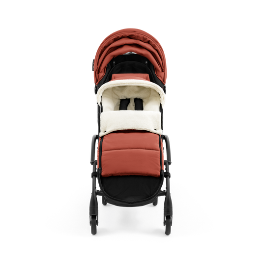 A stroller with a rust-colored padded footmuff, cream fleece lining, and a black frame, shown from the front on a white background.