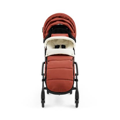 A stroller with a rust-colored padded footmuff, cream fleece lining, and a black frame, shown from the front on a white background.