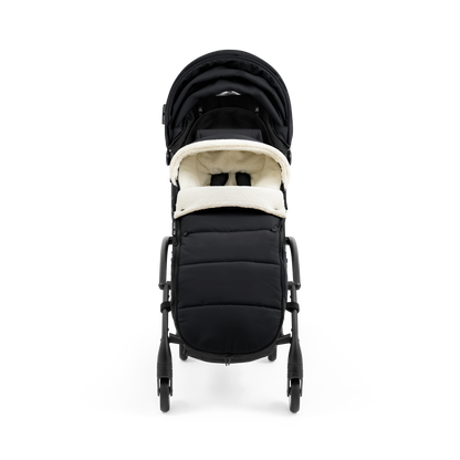 A stroller with a black colored padded footmuff, cream fleece lining, and a black frame, shown from the front on a white background.