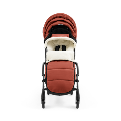 A stroller with a rust-colored padded footmuff, cream fleece lining, and a black frame, shown from the front on a white background.