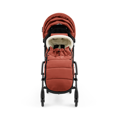 A stroller with a rust-colored padded footmuff, cream fleece lining, and a black frame, shown from the front on a white background.