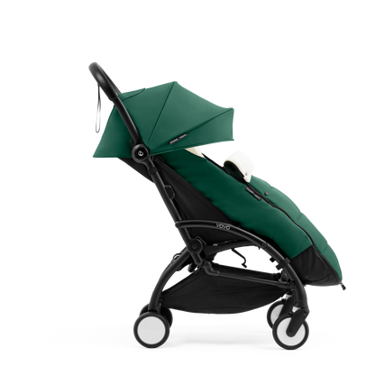 A stroller with a forest green colored padded footmuff, cream fleece lining, and a black frame, shown from the front on a white background.