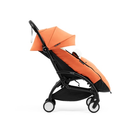 A stroller with a orange colored padded footmuff, cream fleece lining, and a black frame, shown from the front on a white background.