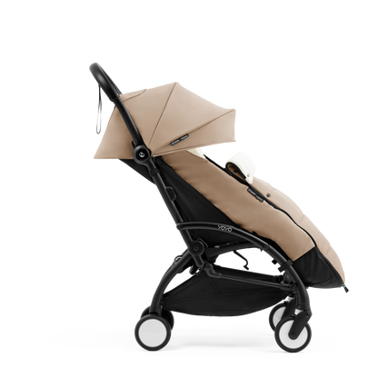 A stroller with a beige colored padded footmuff, cream fleece lining, and a black frame, shown from the front on a white background.