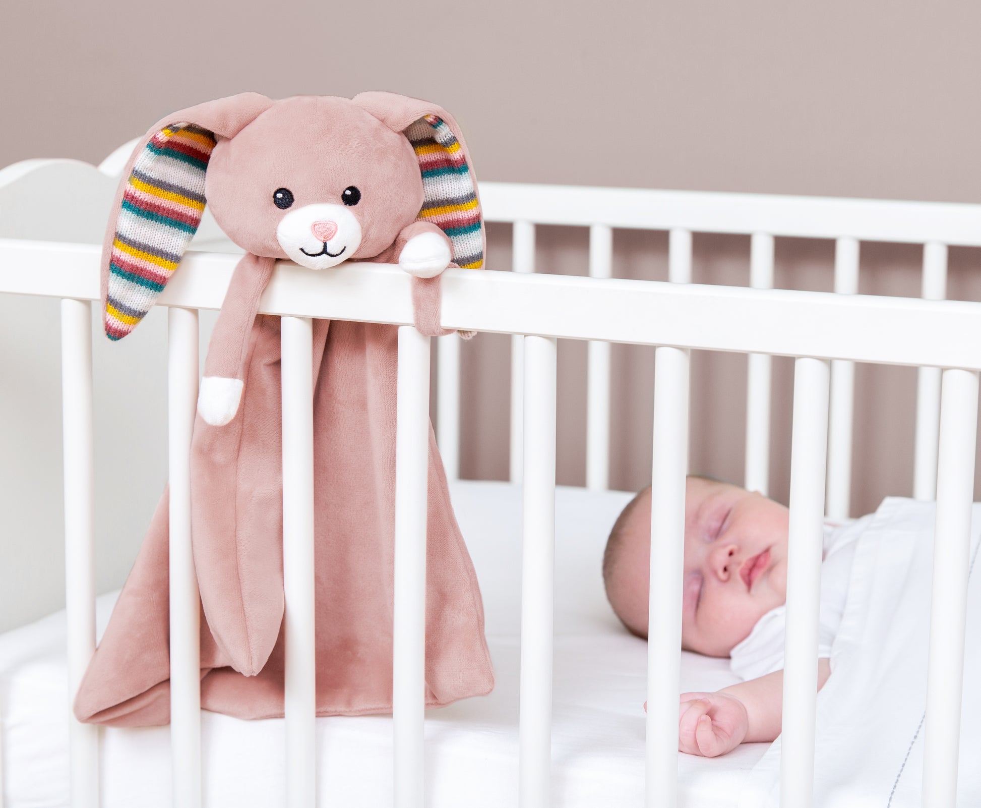 A pink bunny baby comforter attached to a cot bed,  while the baby sleeps.