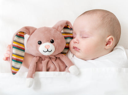 A pink bunny baby comforter resting beside a baby while the baby sleeps.