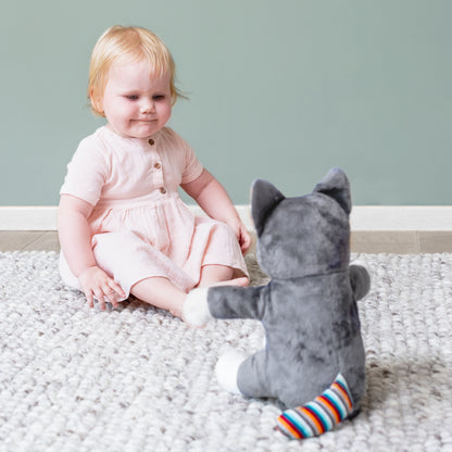 A grey and white shaped cat clapping toy, illustrating its clapping motion and sound, while a toddler plays with it on the floor.