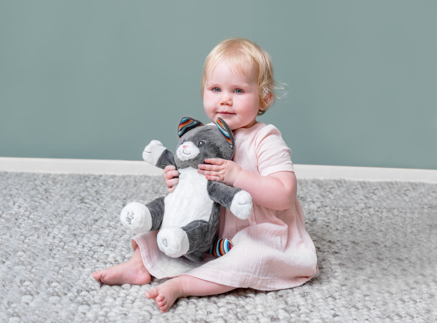 A grey and white shaped cat clapping toy, illustrating its clapping motion and sound, while a holds it on the floor.