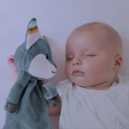 A teal fox baby comforter, resting beside a baby, while the baby sleeps.