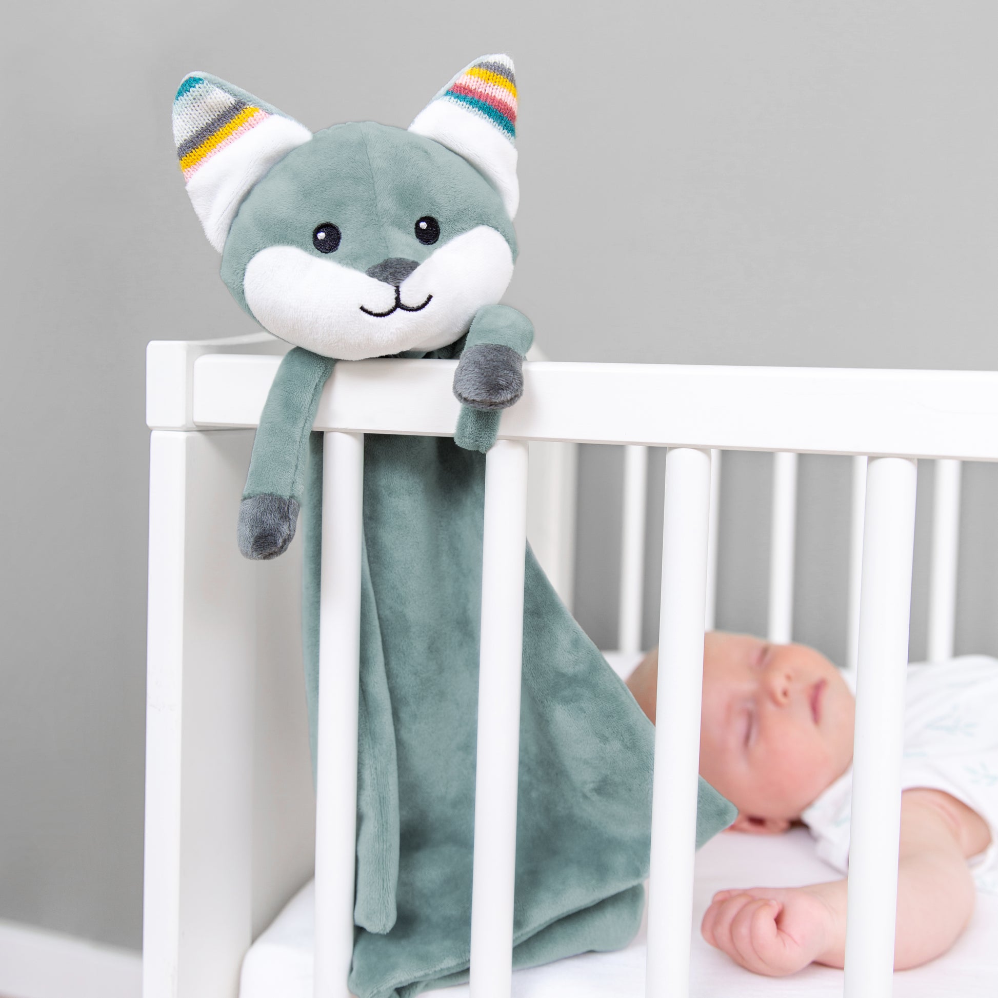 A teal fox baby comforter, attached to a cot bed, while the baby sleeps.