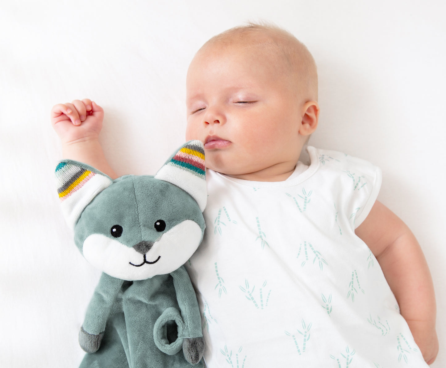 A teal fox baby comforter, resting beside a baby, while the baby sleeps.