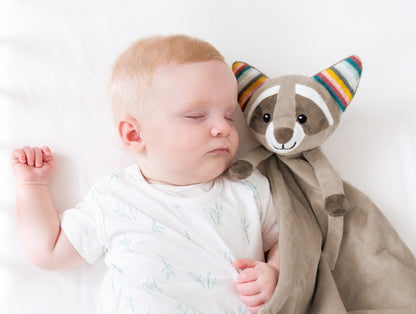 A beige racoon baby comforter lying beside a baby, while the baby sleeps.